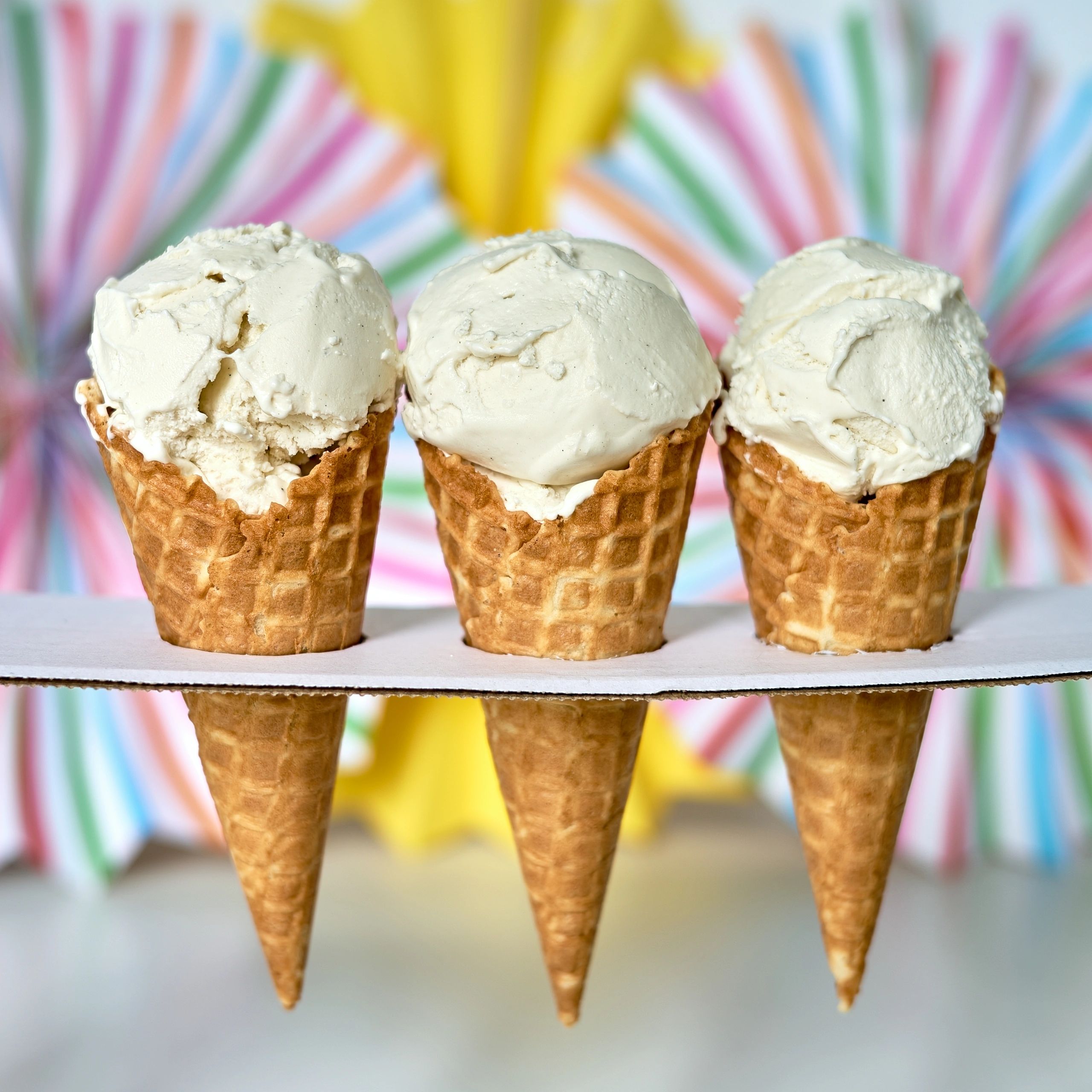 Three vanilla ice cream cones on a colorful background